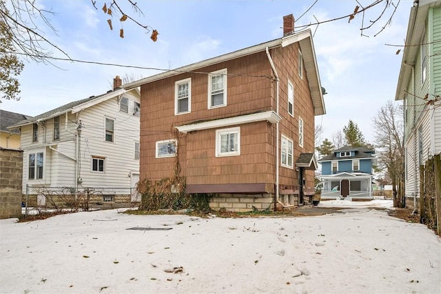 snow covered rear of property featuring a chimney