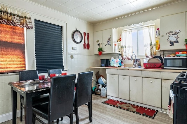 kitchen featuring a sink, black gas stove, white cabinetry, light wood finished floors, and stainless steel microwave