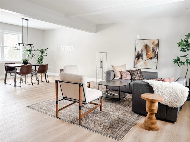 living area featuring vaulted ceiling with beams, light wood-style flooring, and baseboards