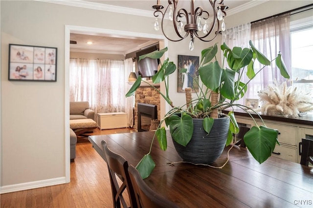 dining space with a chandelier, a fireplace, baseboards, light wood finished floors, and crown molding