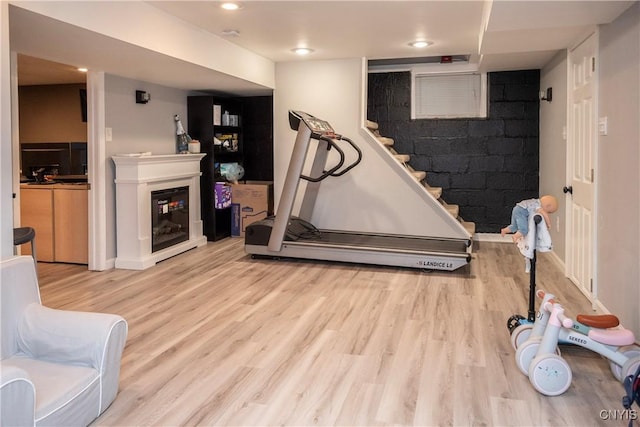 exercise area featuring a glass covered fireplace, light wood-style flooring, and recessed lighting