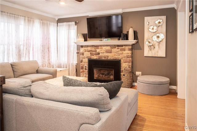 living room with ceiling fan, a fireplace, wood finished floors, baseboards, and crown molding