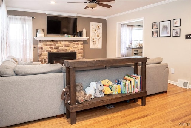 living room featuring visible vents, a ceiling fan, ornamental molding, light wood-type flooring, and a fireplace