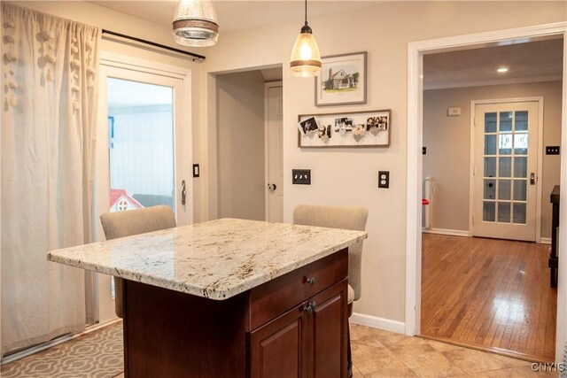 kitchen with baseboards, a kitchen island, a kitchen breakfast bar, dark brown cabinets, and pendant lighting