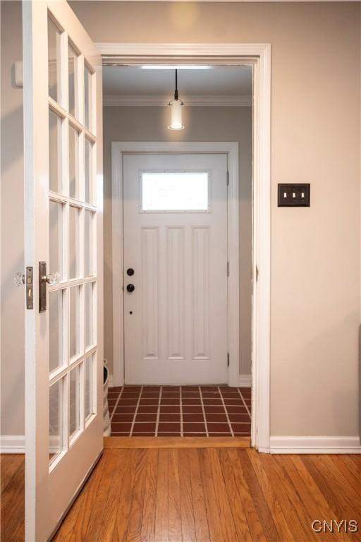 doorway featuring baseboards, wood finished floors, and crown molding