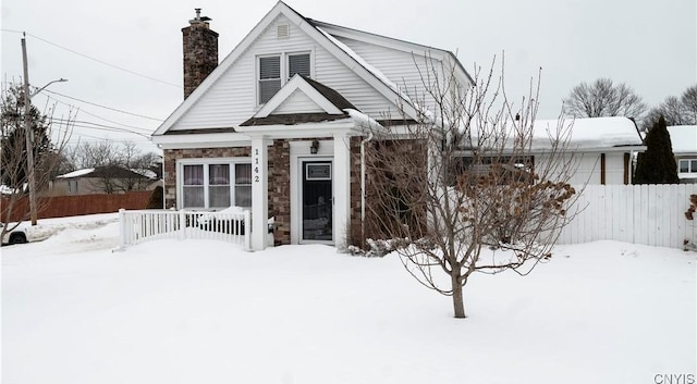 view of front of property featuring stone siding, a chimney, and fence