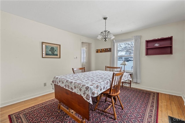 dining space with wood-type flooring, visible vents, baseboards, and an inviting chandelier