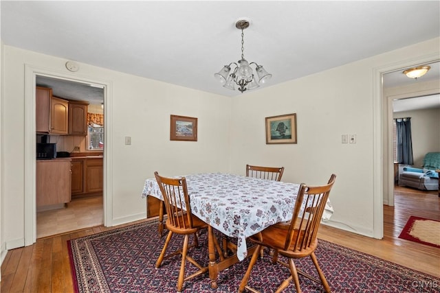 dining space with light wood-style flooring, baseboards, and a notable chandelier