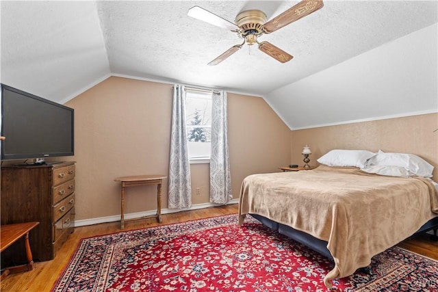 bedroom with a textured ceiling, vaulted ceiling, wood finished floors, and baseboards