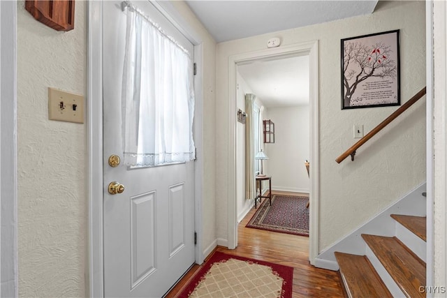 doorway to outside featuring wood finished floors, a textured wall, baseboards, and stairs