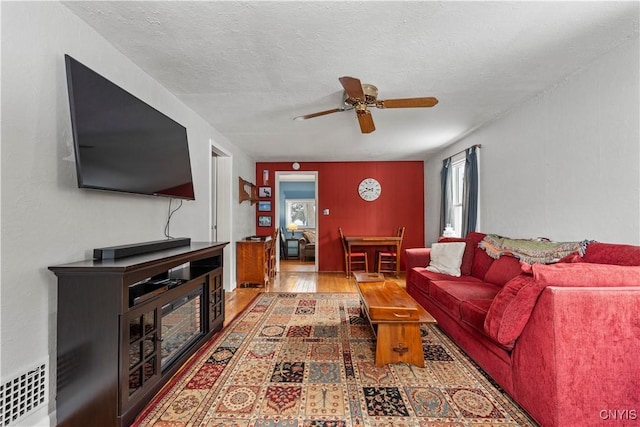 living room with a textured ceiling, wood finished floors, visible vents, and a ceiling fan