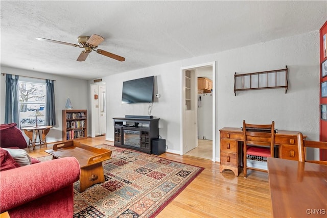 living room with a glass covered fireplace, ceiling fan, a textured ceiling, wood finished floors, and baseboards