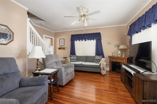 living room featuring ceiling fan, a fireplace, wood finished floors, stairway, and crown molding