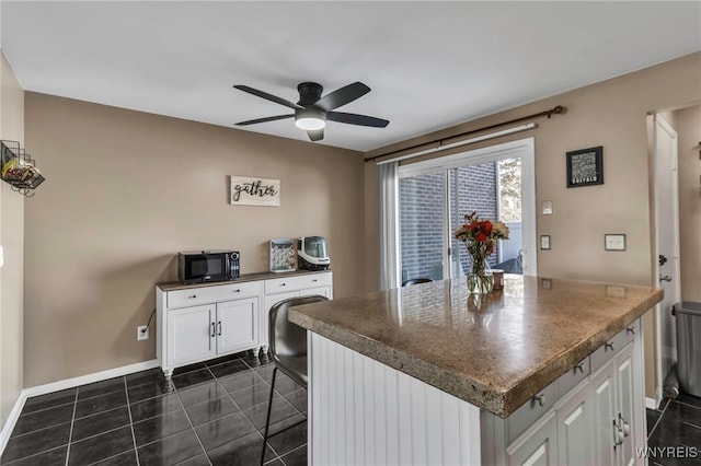 kitchen with white cabinets, dark countertops, a kitchen breakfast bar, dark tile patterned floors, and black microwave