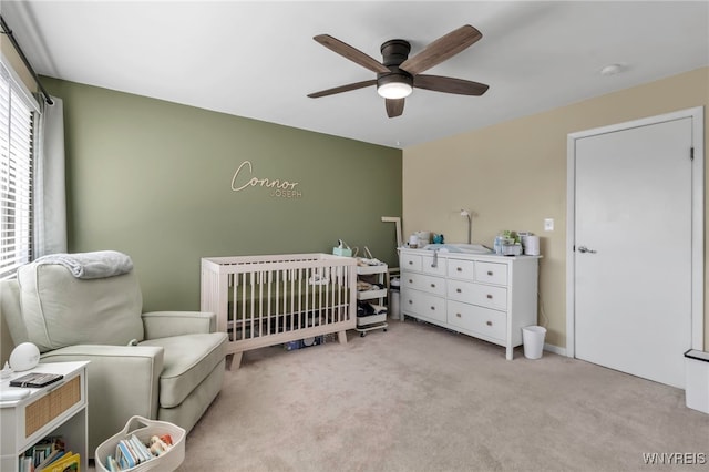 bedroom featuring light carpet, ceiling fan, and a nursery area