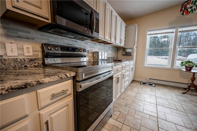 kitchen with appliances with stainless steel finishes, baseboard heating, backsplash, stone finish floor, and dark stone countertops