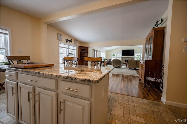 kitchen featuring light stone counters, open floor plan, vaulted ceiling, stone tile flooring, and white cabinetry