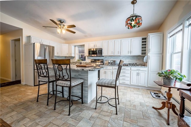 kitchen with a kitchen island, light stone counters, hanging light fixtures, stainless steel appliances, and white cabinetry