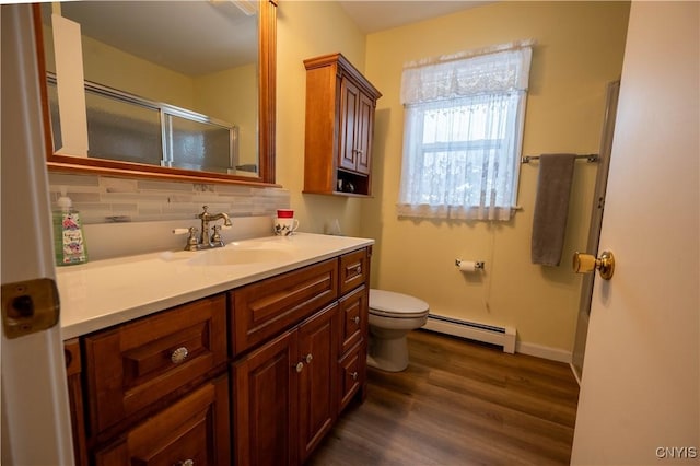 bathroom featuring toilet, a baseboard heating unit, wood finished floors, vanity, and backsplash