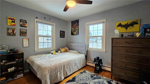 bedroom with ceiling fan, multiple windows, a baseboard radiator, and wood finished floors