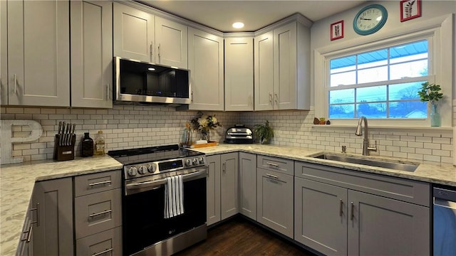 kitchen with gray cabinetry, stainless steel appliances, a sink, decorative backsplash, and dark wood-style floors