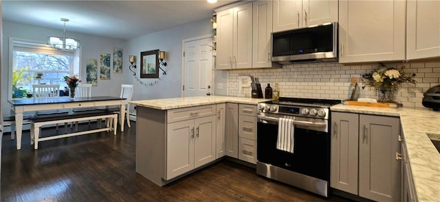 kitchen with dark wood-style floors, tasteful backsplash, appliances with stainless steel finishes, light stone countertops, and a peninsula