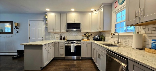 kitchen with light stone counters, a baseboard heating unit, stainless steel appliances, a peninsula, and a sink