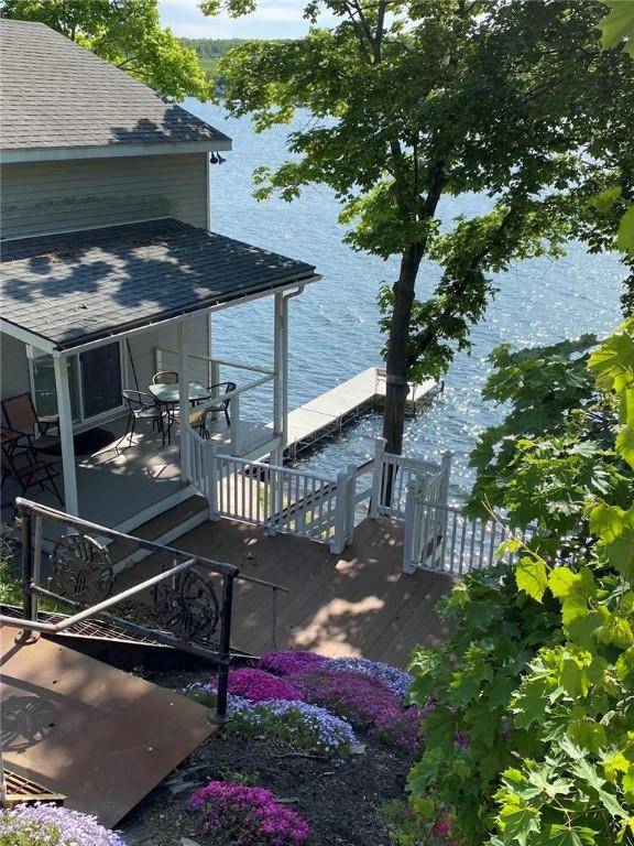 exterior space with a shingled roof, a dock, and a water view