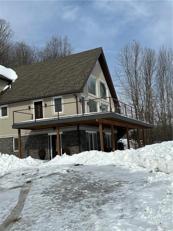 snow covered house featuring stone siding and a balcony