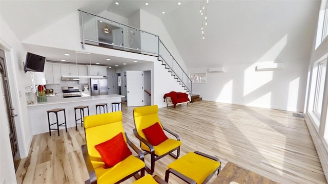 interior space featuring stairs, an AC wall unit, light wood finished floors, and high vaulted ceiling