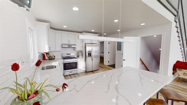 kitchen with white cabinets, appliances with stainless steel finishes, a peninsula, under cabinet range hood, and a sink