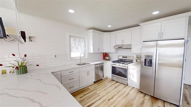 kitchen featuring light stone counters, stainless steel appliances, white cabinetry, a sink, and under cabinet range hood