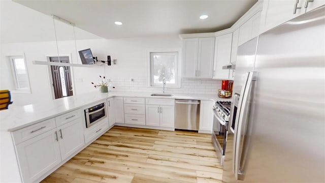 kitchen featuring a peninsula, white cabinetry, appliances with stainless steel finishes, light wood finished floors, and tasteful backsplash