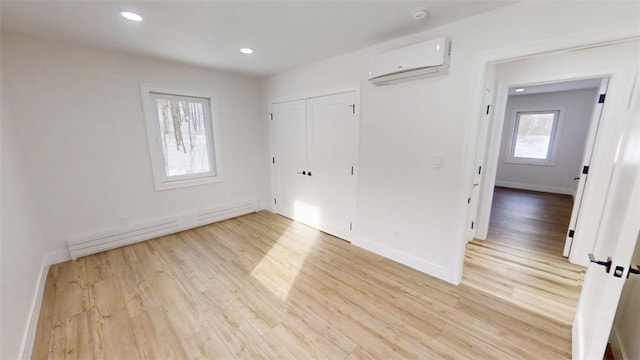 unfurnished bedroom with a baseboard radiator, recessed lighting, baseboards, light wood-type flooring, and a wall mounted air conditioner