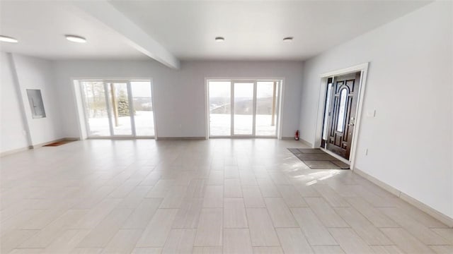 unfurnished room featuring light wood-style flooring, beamed ceiling, a wealth of natural light, and baseboards