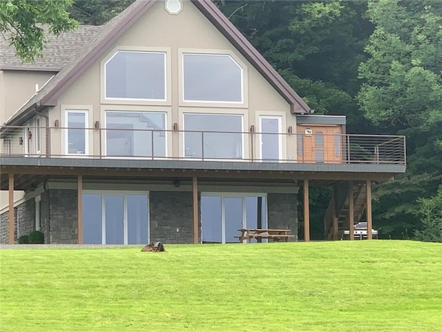 back of property featuring stone siding, stairway, a lawn, and stucco siding