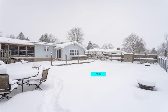 snowy yard featuring fence, a deck, an outdoor structure, and a storage unit