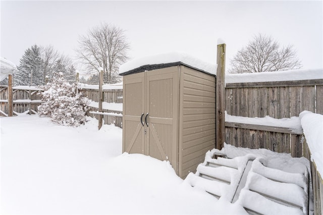 snow covered structure with a shed, a fenced backyard, and an outdoor structure