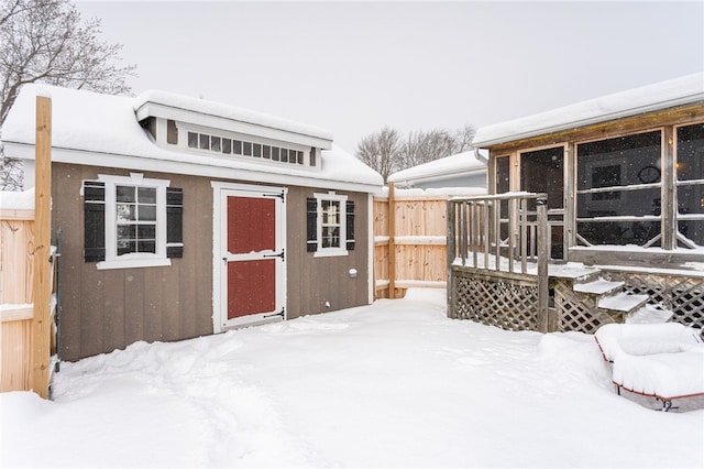 snow covered structure with a storage shed, fence, and an outdoor structure