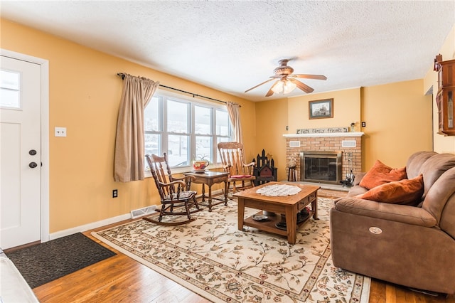 living room with a brick fireplace, baseboards, visible vents, a textured ceiling, and light wood-style floors