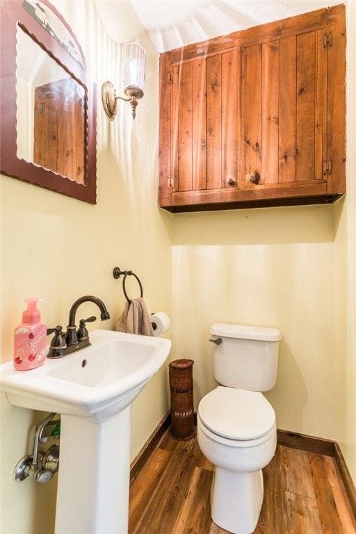 half bathroom featuring toilet, baseboards, and wood finished floors