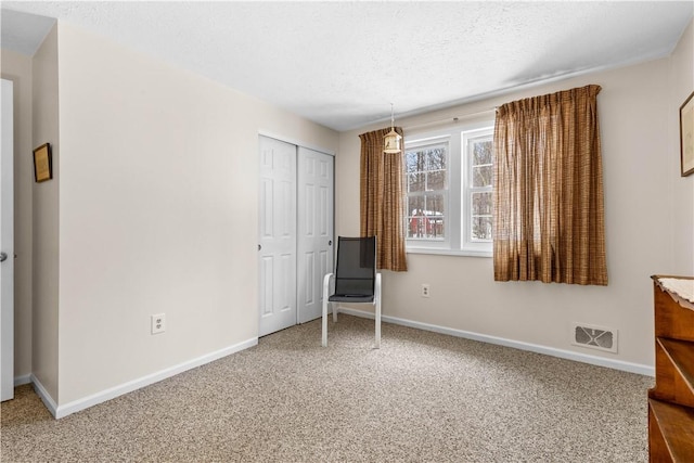 unfurnished room featuring a textured ceiling, carpet, visible vents, and baseboards