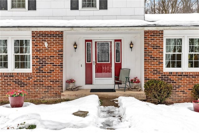 snow covered property entrance with brick siding