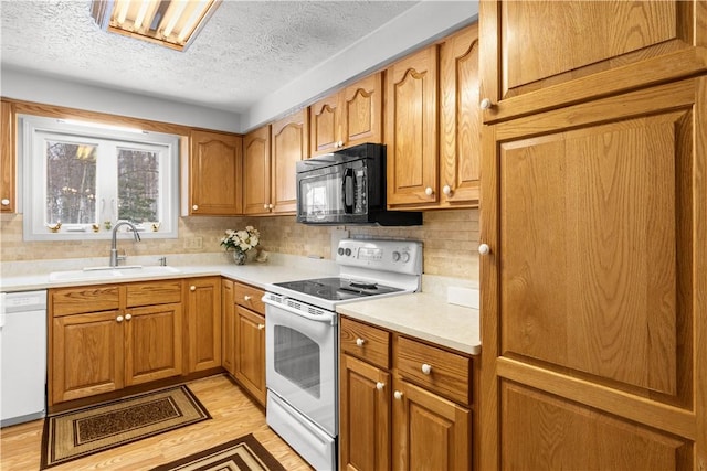 kitchen featuring white appliances, light wood-style flooring, brown cabinets, light countertops, and a sink