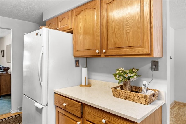 kitchen featuring a textured ceiling, wood finished floors, baseboards, light countertops, and freestanding refrigerator