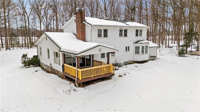 snow covered rear of property with a garage and a chimney