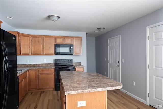 kitchen with baseboards, black appliances, light wood finished floors, and a center island