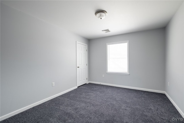 spare room featuring dark colored carpet, visible vents, and baseboards