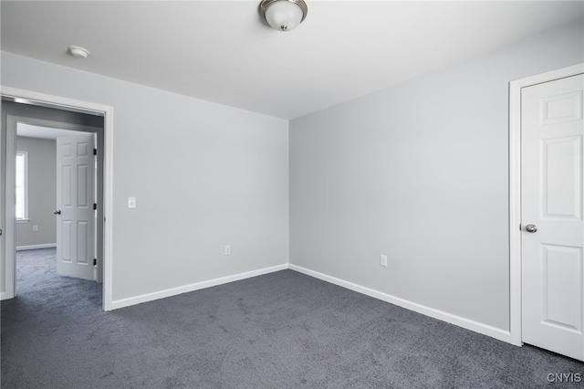 empty room featuring dark colored carpet and baseboards