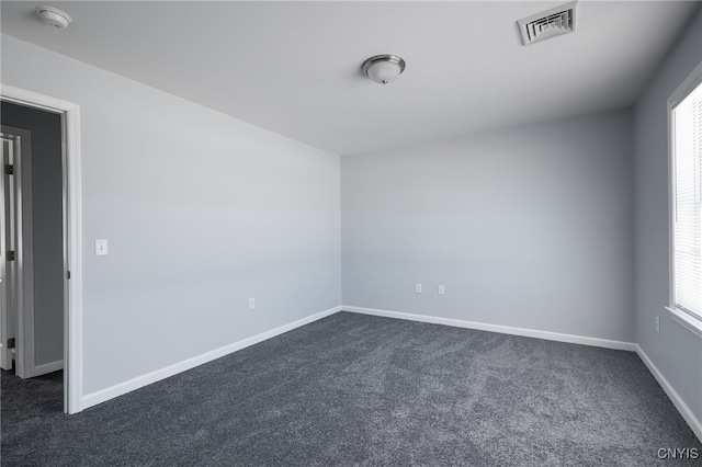 spare room with a healthy amount of sunlight, visible vents, and dark carpet